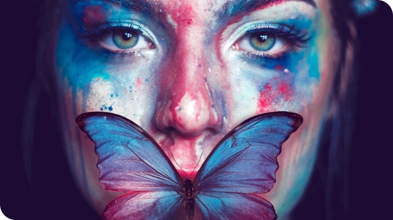 Ansikt malt i mange farger med en sommerfugl over munn